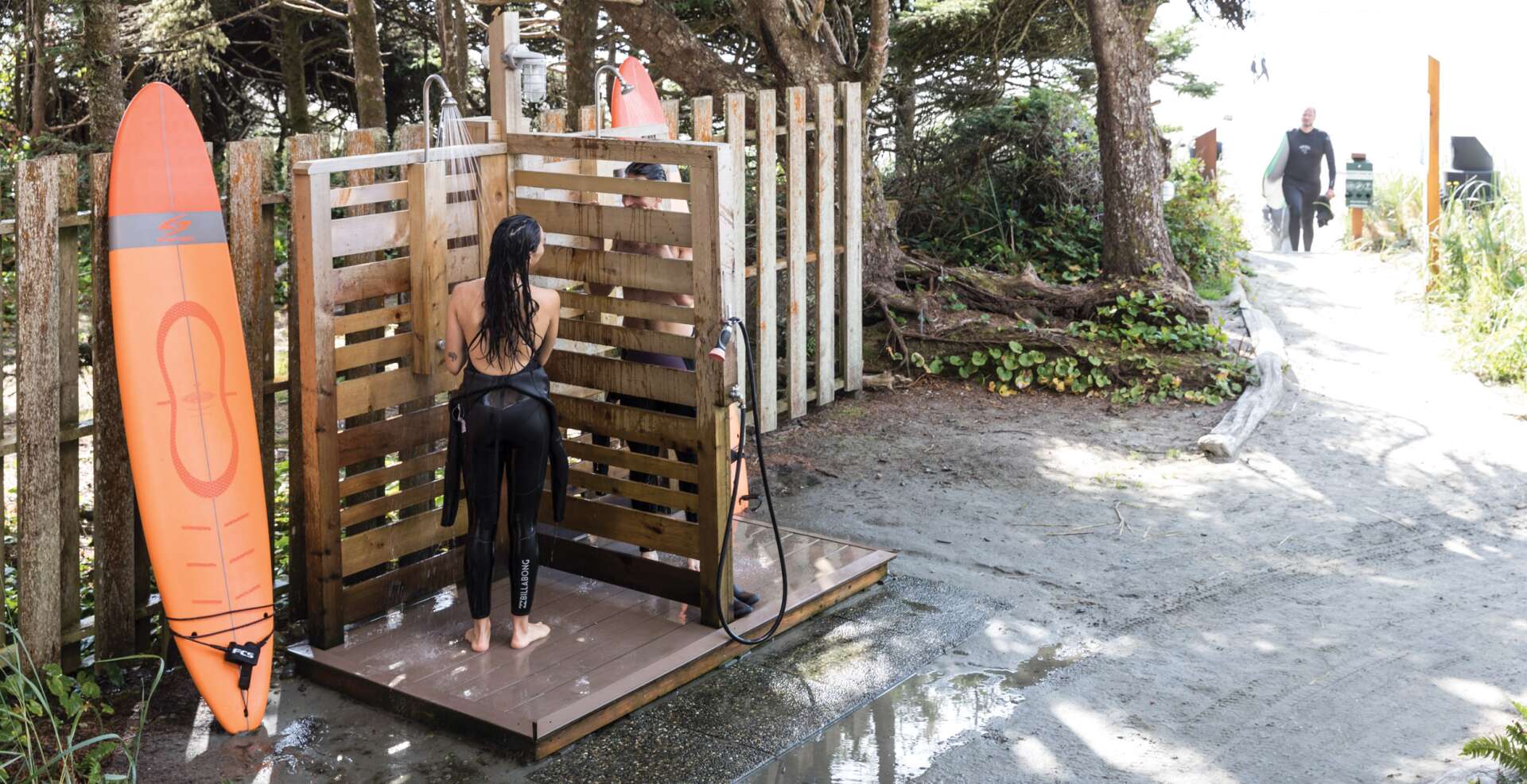 Girl showing in her wet suit after surfing and other surfers coming up from beach.